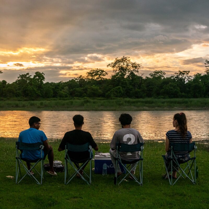 Four people sitting on camping chairs in front of the river at sunset time